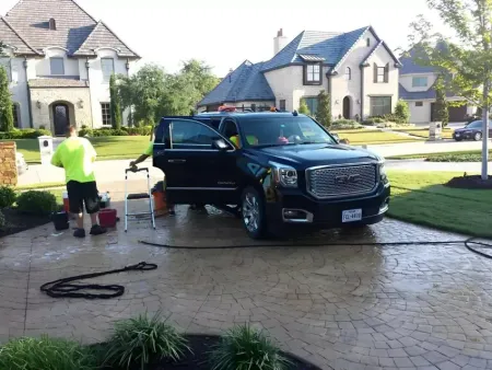 Detailer washing a black GMC Yukon Denali on a customer's paver driveway